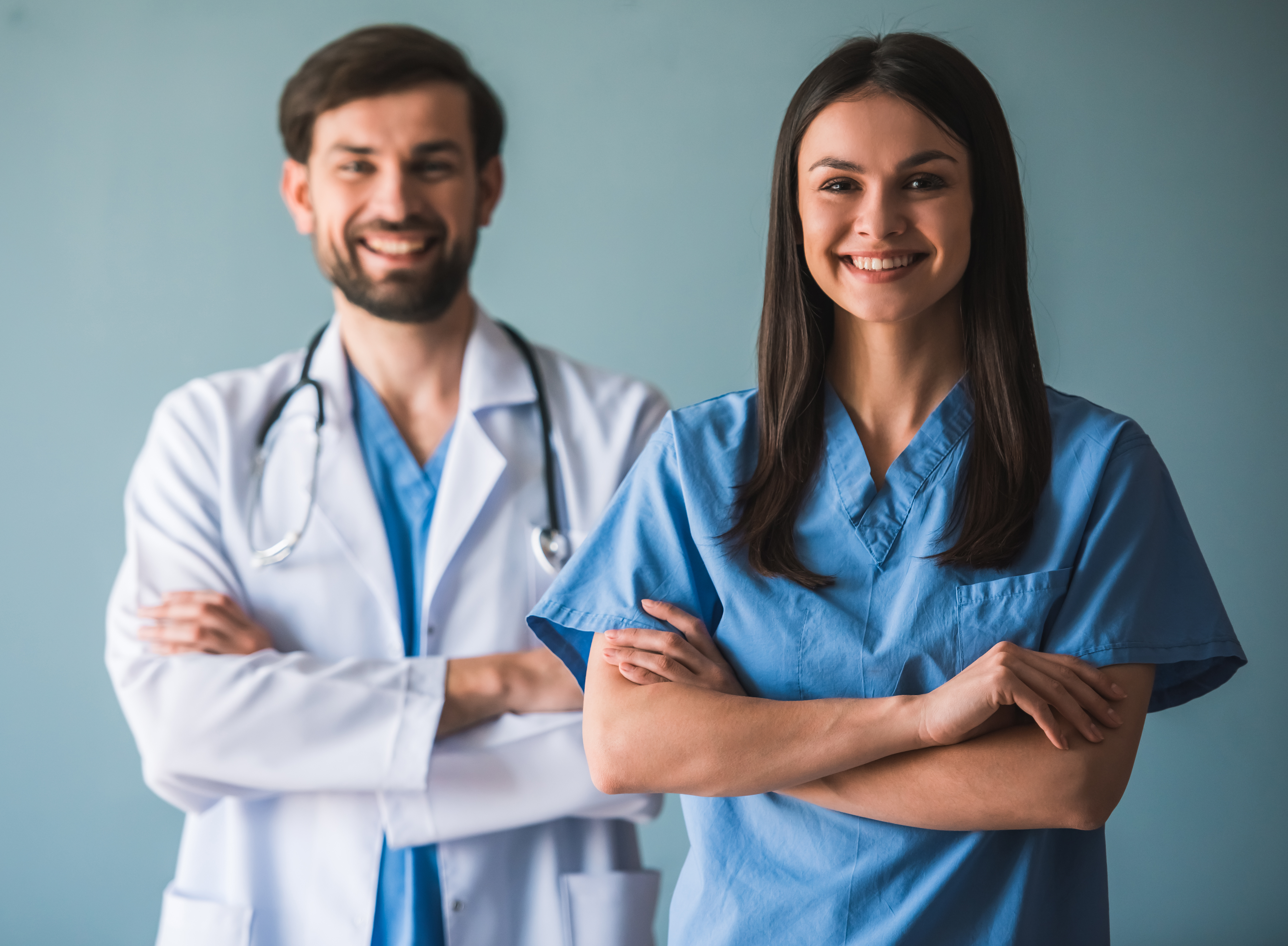 young doctors are looking at camera and smiling while standing with crossed arms on blue background